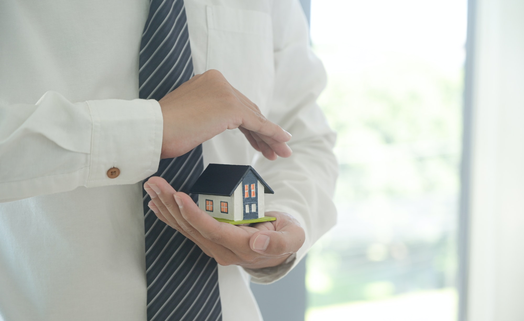 Insurance agent hold a house model in hand showing the symbol of home insurance.